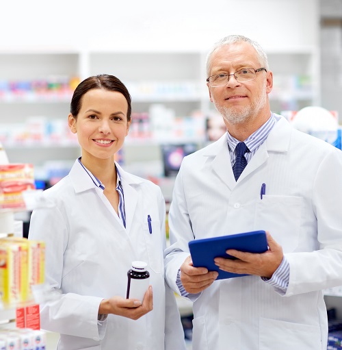 female pharmacist holding bottle, standing with male colleague holding blue tablet
