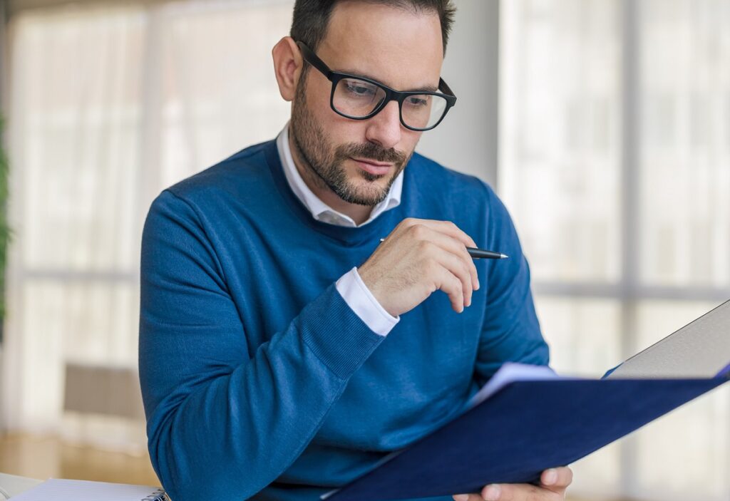 man in blue sweater and glasses reading a memo
